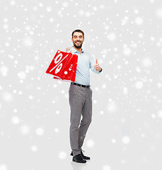 Image showing smiling man with red shopping bags over snow