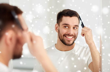 Image showing happy man brushing hair with comb at bathroom