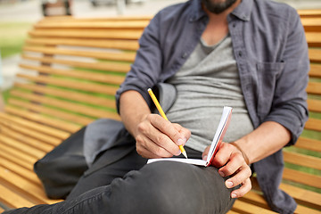 Image showing close up of man writing to notebook on city street