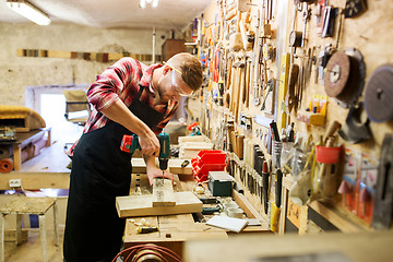 Image showing carpenter with drill drilling plank at workshop