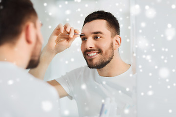 Image showing man with tweezers tweezing eyebrow at bathroom