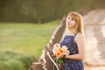 Image showing Young girl with a bouquet of roses standing on the bridge in the background blurred foliage