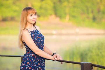 Image showing The charming young girl standing on a rustic bridge over the river at dawn sun