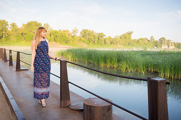 Image showing The charming young girl walking on the bridge over the river at dawn