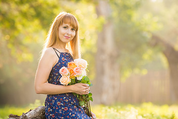 Image showing Beautiful young woman looking with a bouquet of roses in hands on a background of green sunny blurred