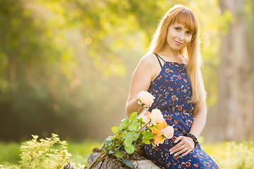 Image showing Beautiful young girl on the background of the sunny blurred greenery, lies next to a bouquet of roses