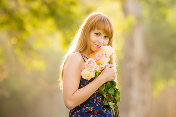 Image showing Beautiful young sexy girl standing with a bouquet of roses on a background of green sunny blurred