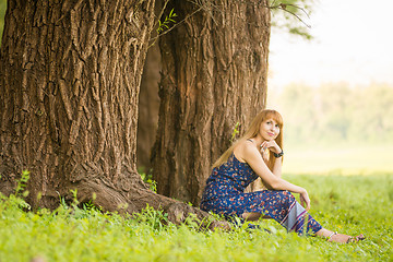 Image showing Beautiful young woman sat on the roots of the old large tree and looked up dreamily
