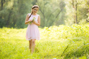 Image showing Young girl in the summer light dress collecting wild flowers