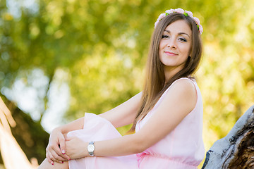 Image showing Beautiful girl sits on a background illuminated by the sun leaves