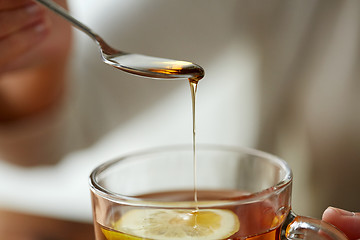 Image showing close up of woman adding honey to tea with lemon