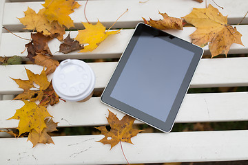 Image showing tablet pc and coffee cup on bench in autumn park