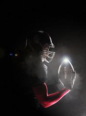 Image showing American football player posing with ball on black background