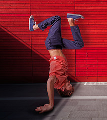 Image showing Break dancer doing handstand against red wall background