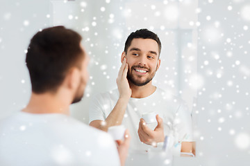 Image showing happy young man applying cream to face at bathroom