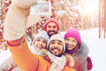 Image showing smiling friends with camera in winter forest