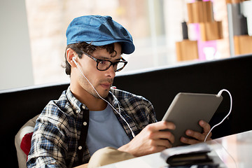 Image showing man with tablet pc and earphones sitting at cafe