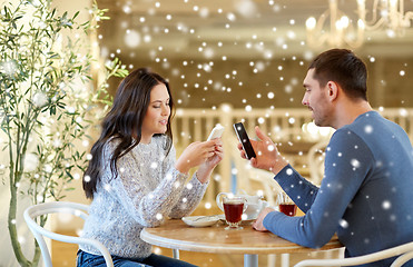 Image showing happy couple with smartphones drinking tea at cafe