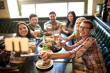 Image showing happy friends with selfie stick at bar or pub