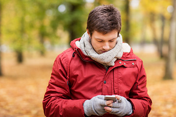 Image showing young man with smartphone walking at autumn park