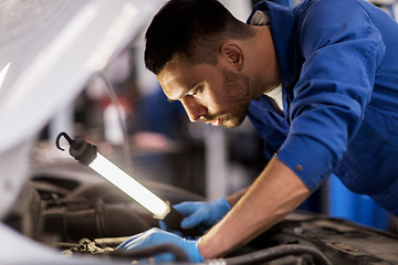 Image showing mechanic man with lamp repairing car at workshop