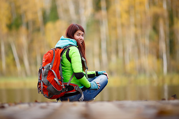 Image showing Brunette with backpack sitting on bridge at lake