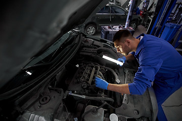 Image showing mechanic man with lamp repairing car at workshop