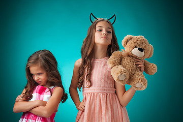 Image showing The two cute little girls on blue background with Teddy bear