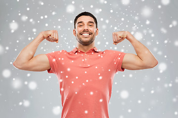 Image showing smiling man showing biceps over snow background