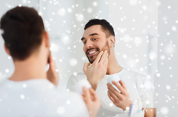 Image showing happy young man applying cream to face at bathroom