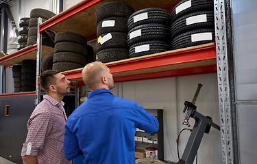 Image showing mechanic and man choosing tires at car shop
