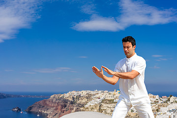 Image showing Handsome man practicing Tai Chi of the rooftops in Oia Santorini