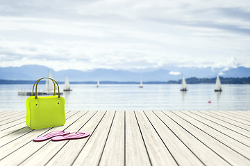 Image showing green bag on a wooden jetty with sailing boats in the background