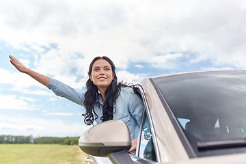 Image showing happy young woman driving in car and waving hand