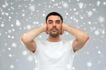 Image showing young man covering his ears with hands over snow