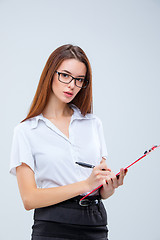 Image showing The young business woman with pen and tablet for notes on gray background