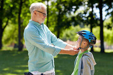 Image showing old man helping boy with bike helmet at park