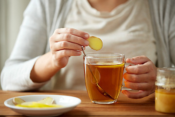 Image showing close up of woman adding ginger to tea with lemon