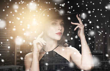 Image showing beautiful woman in black hat over city and snow