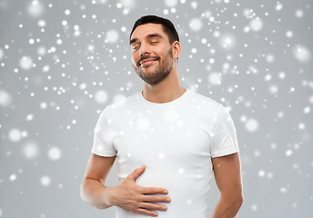 Image showing happy full man touching tummy over snow background