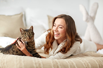 Image showing happy young woman with cat lying in bed at home