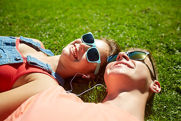 Image showing happy teenage couple with earphones lying on grass