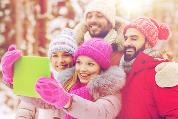 Image showing smiling friends with tablet pc in winter forest