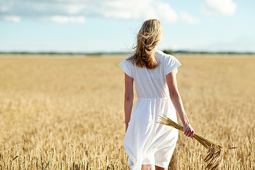 Image showing young woman with cereal spikelets walking on field