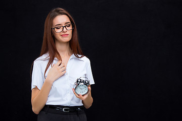 Image showing The young business woman with alarm clock on black background