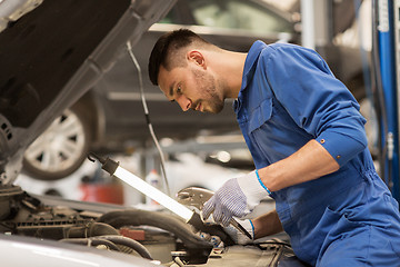 Image showing mechanic man with lamp repairing car at workshop