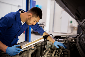 Image showing mechanic man with lamp repairing car at workshop