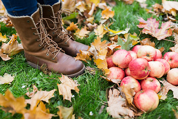 Image showing woman feet in boots with apples and autumn leaves