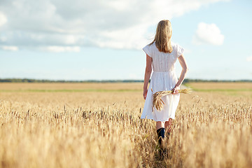 Image showing young woman with cereal spikelets walking on field