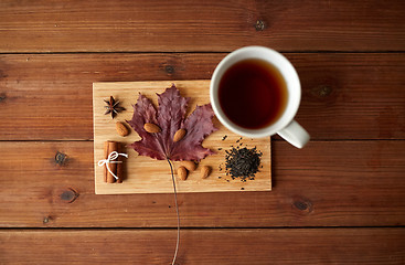 Image showing cup of tea, maple leaf and almond on wooden board